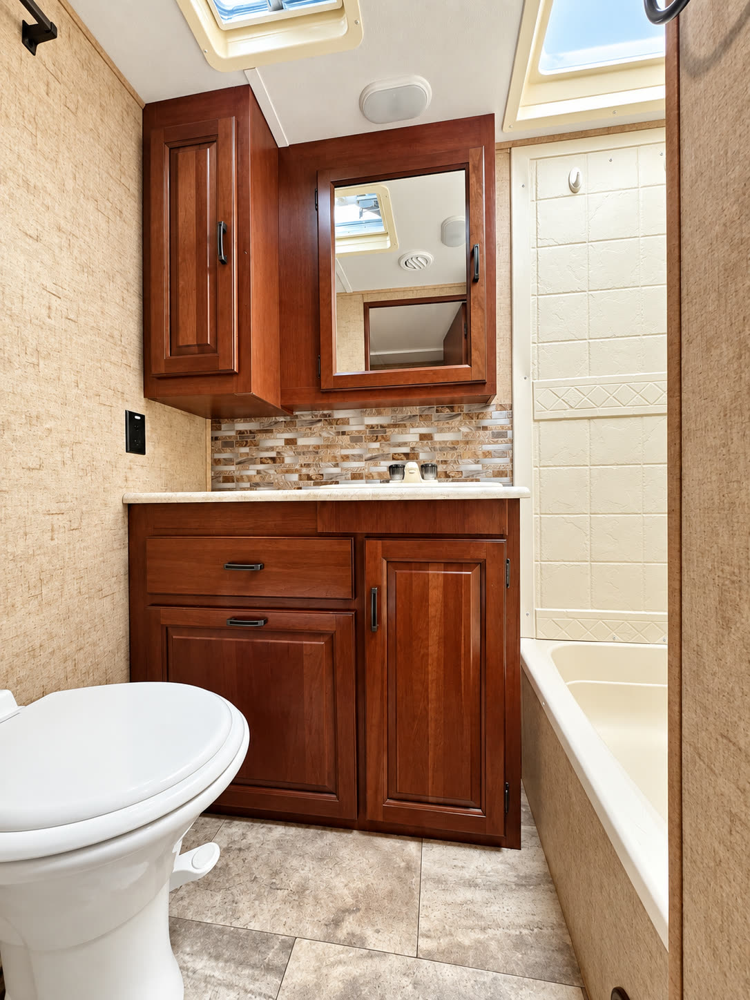 RV bathroom with wood vanity, mirrored cabinet, toilet, and cream shower surround.
