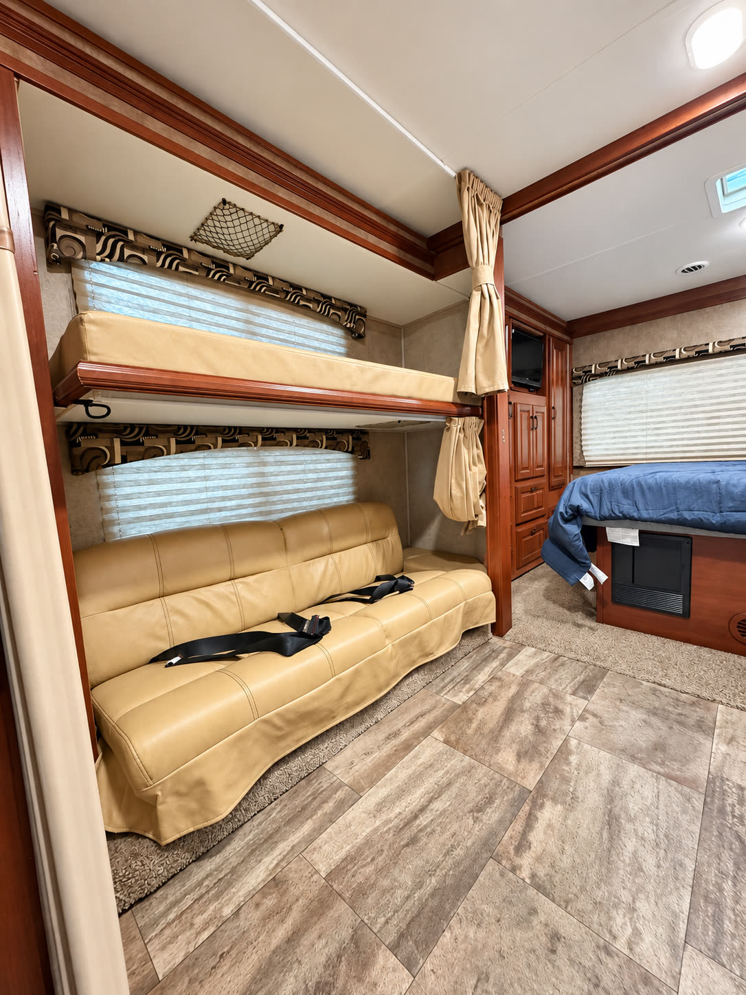 RV sleeping area showing an overhead bunk above a tan sofa and the rear bedroom beyond.
