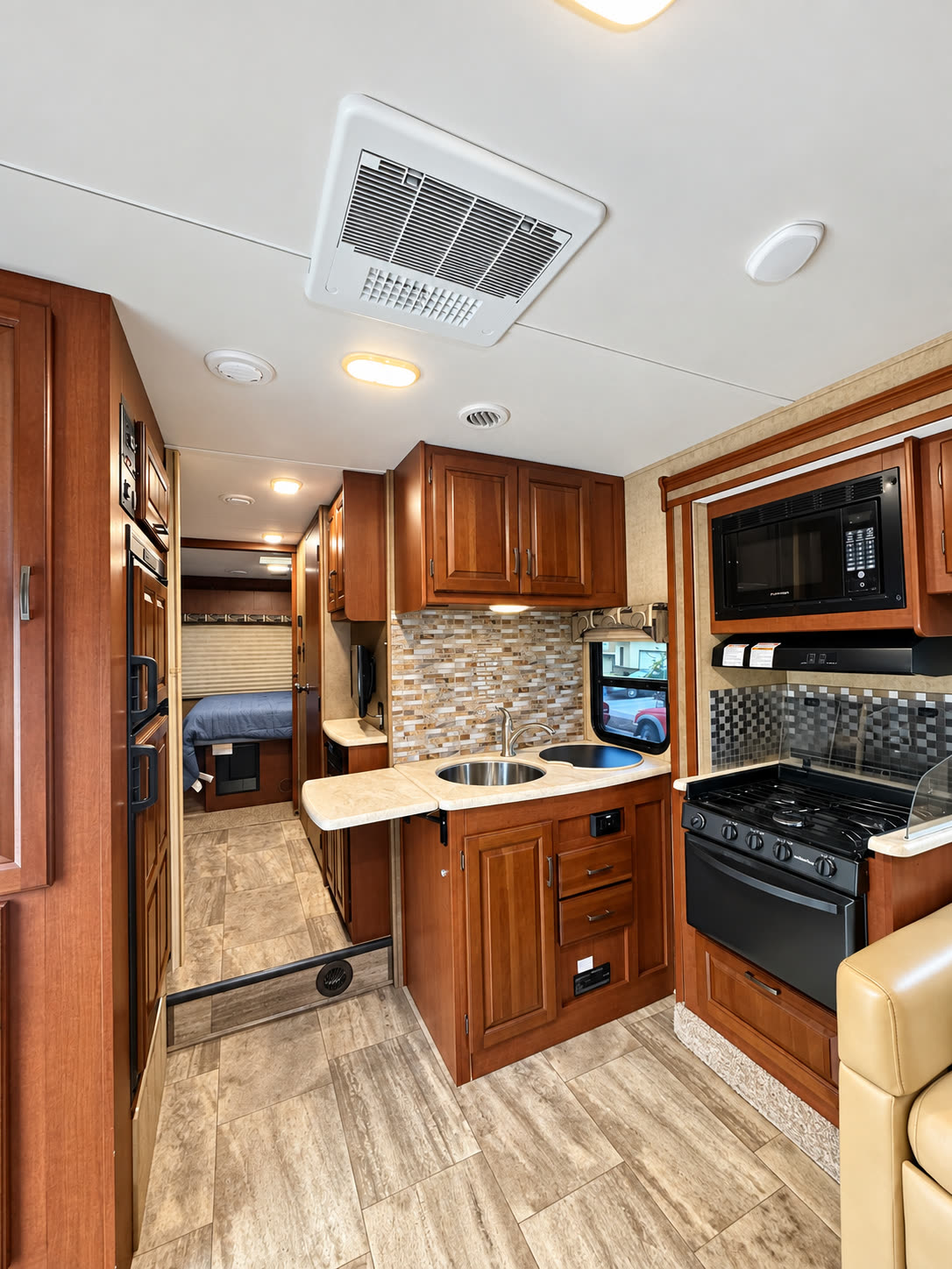 RV kitchen with double sink, wood cabinetry, microwave, gas range, and hallway to the bed.